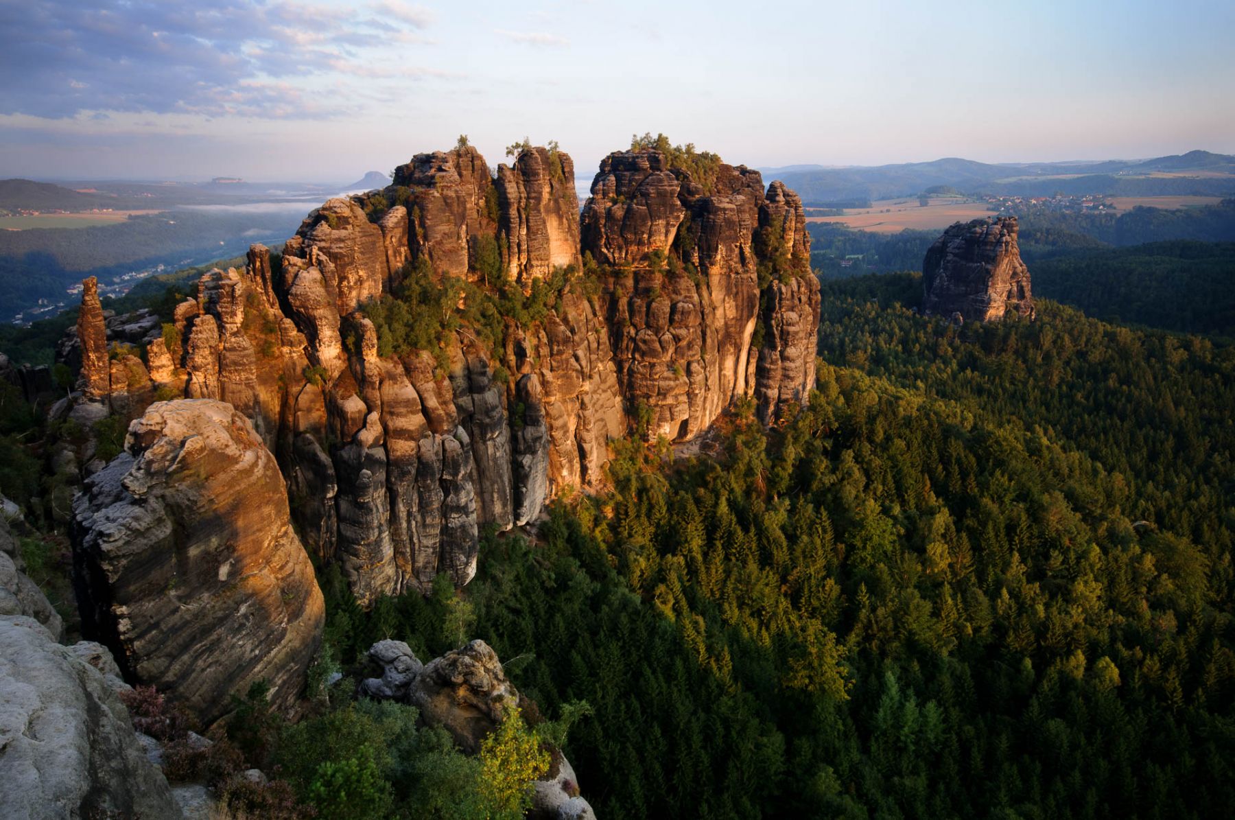 Im Elbsandsteingebirge ragen die imposanten Schrammsteine aus üppigen Wäldern empor. Diese markanten Sandsteinformationen befinden sich in Deutschland, Europa und bieten einen beeindruckenden Blick auf die umgebende Landschaft. Imposante Sandsteinfelsen der Schrammsteine im Elbsandsteingebirge bei Sonnenaufgang.