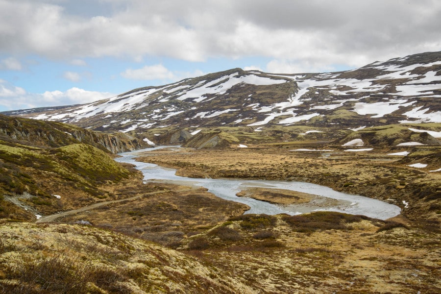Weite norwegische Landschaft mit Fluss und schneebedeckten Bergen im Dovrefjell.