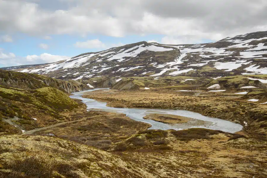 Weite norwegische Landschaft mit Fluss und schneebedeckten Bergen im Dovrefjell.