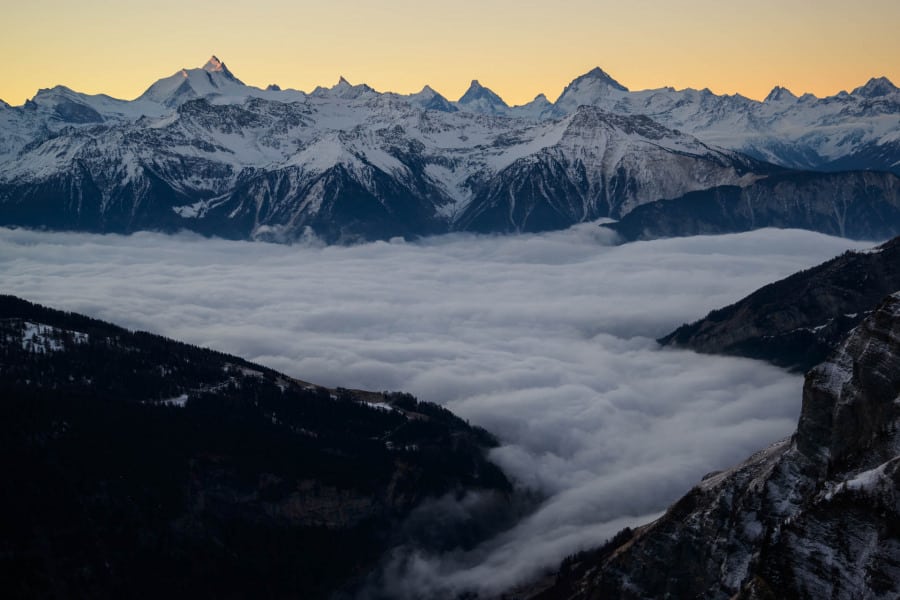 Verschneite Alpenberge im Wallis, darüber eine Wolkendecke bei Dämmerung.