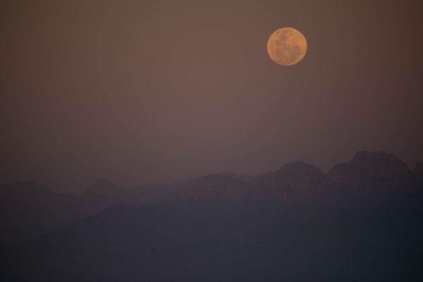 Vollmond steigt über eine Bergsilhouette in Südafrika in der Abenddämmerung auf.