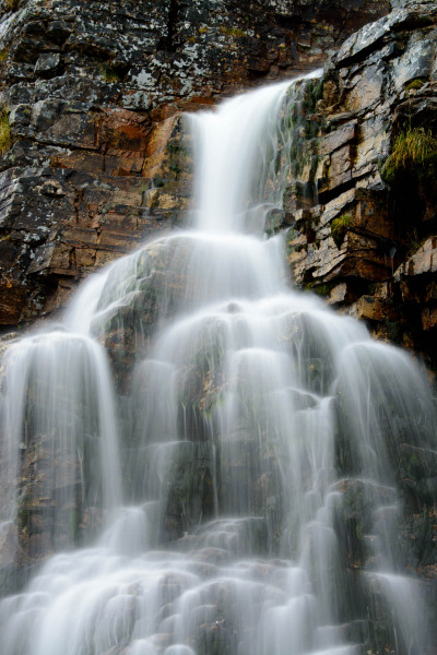 Ein mehrstufiger Wasserfall fließt über schichtartige Felsen in Norwegen.