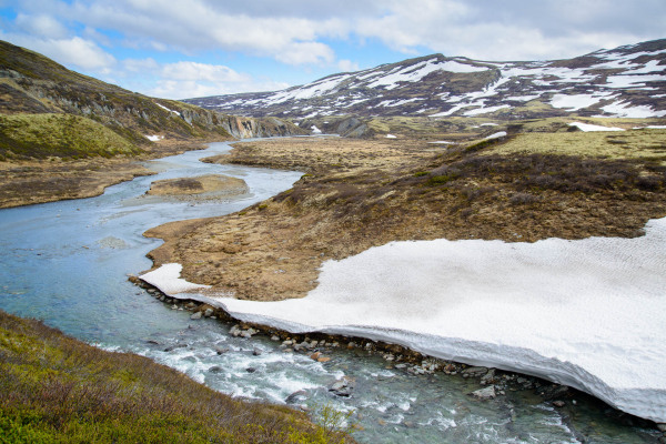Alpine Flusslandschaft im Dovrefjell mit schmelzendem Schnee und Hügeln.