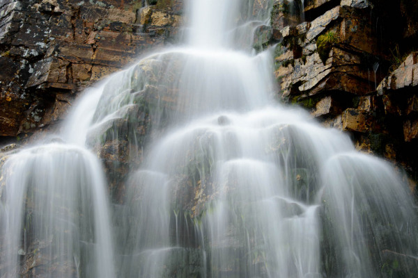 Ein mehrstufiger Wasserfall fließt über schichtartige Felsen in Norwegen.
