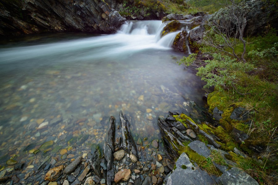 Ein klarer Gebirgsbach fließt zwischen moosbedeckten Felsen in Norwegen.