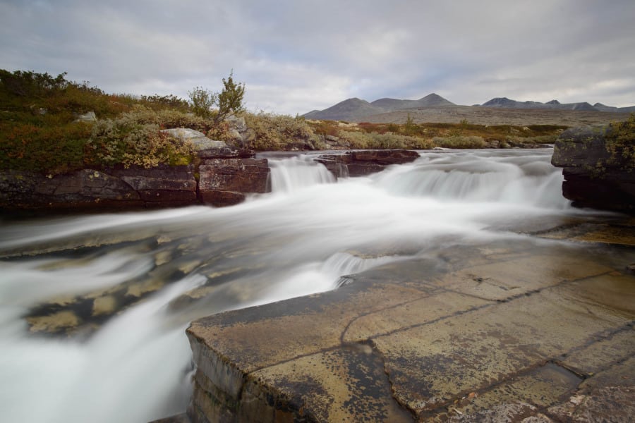 Dynamisch fließender Fluss in felsiger Landschaft der Rondane-Bergen, Norwegen.