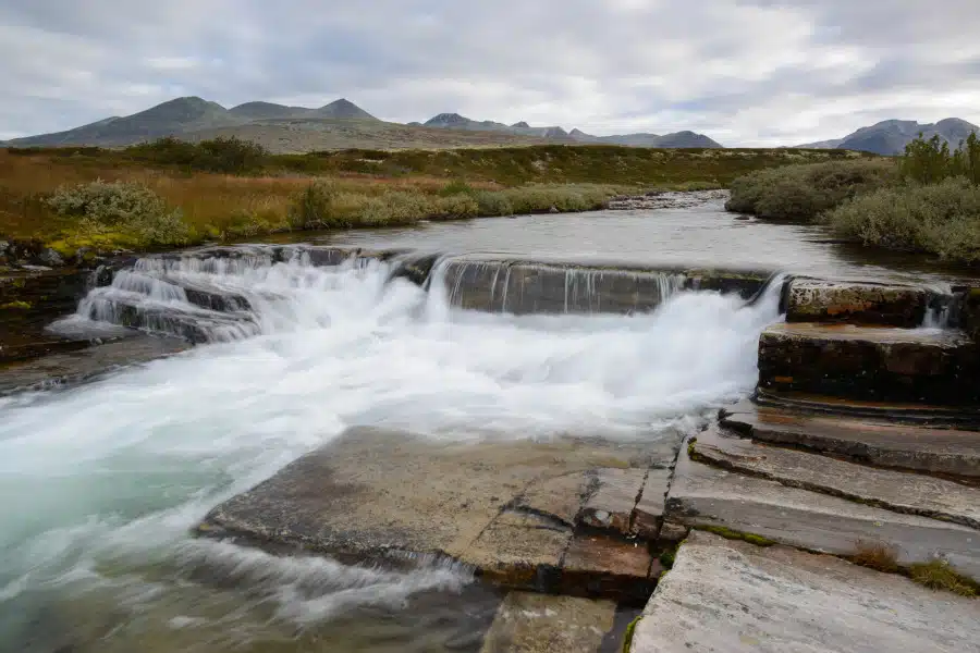 Kleiner Wasserfall mit flachen Felsen im Rondane Nationalpark, Norwegen, umgeben von Bergen.