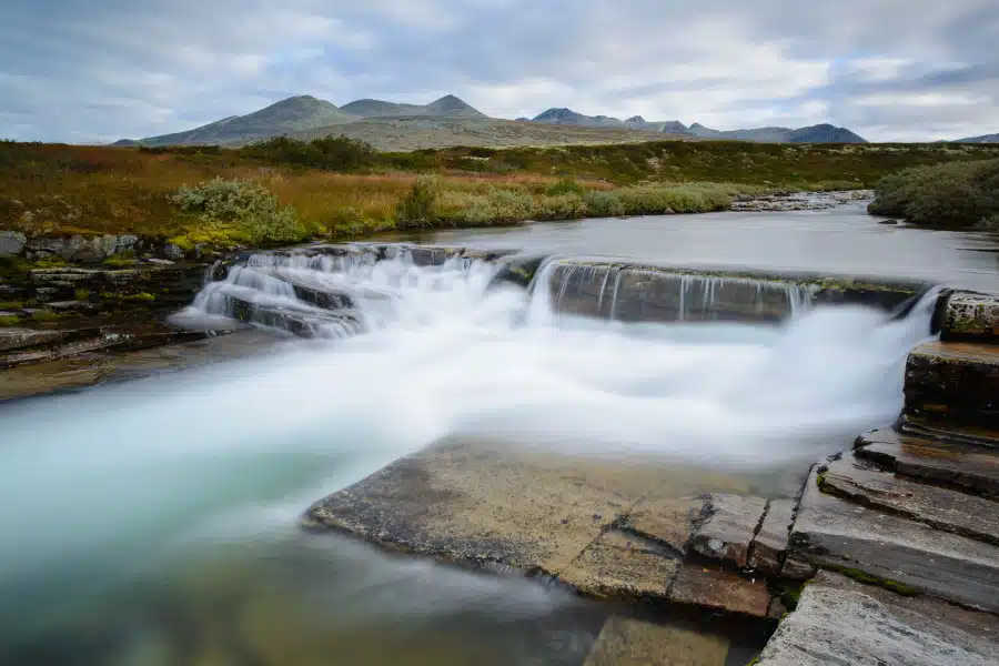 Sanft fließender Wasserfall in skandinavischer Landschaft mit Hügeln.