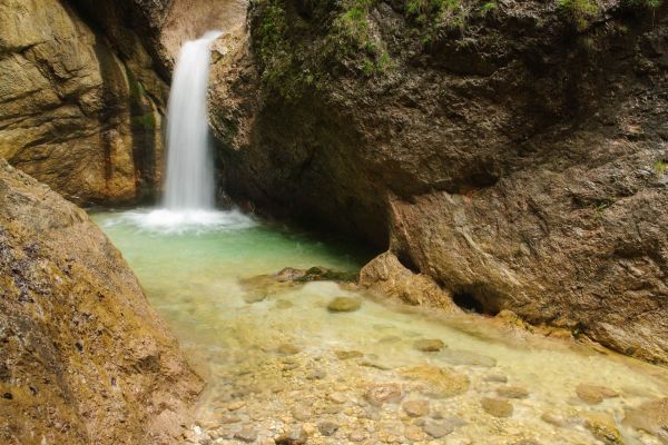 Kleiner Wasserfall fließt in klaren Bergbach umgeben von Felsen.
