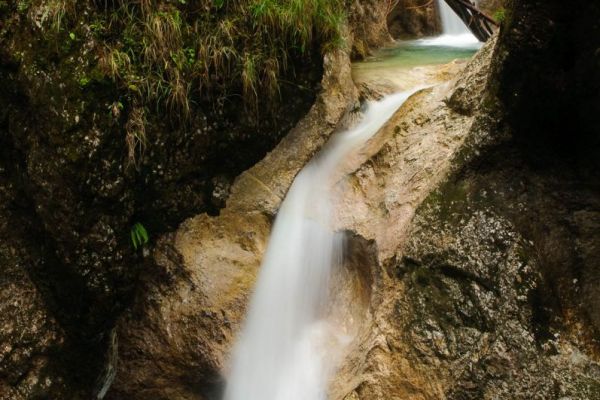 Kleiner Wasserfall fließt durch steinige Schlucht in der Almbachklamm.