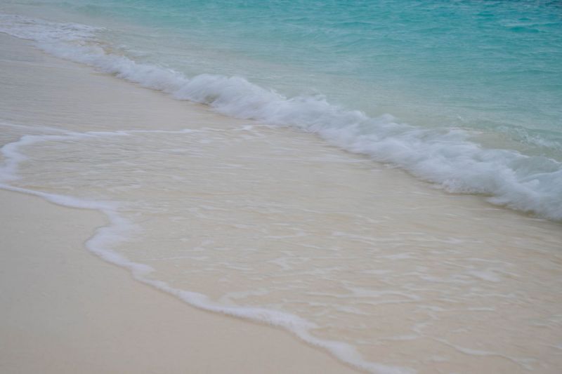 Sanfte Wellen treffen auf einen tropischen Sandstrand mit türkisfarbenem Wasser.
