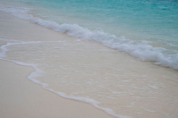 Sanfte Wellen treffen auf einen tropischen Sandstrand mit türkisfarbenem Wasser.