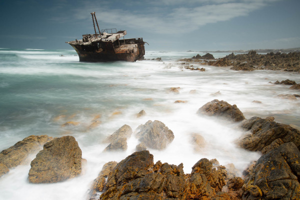 Ein verrostetes Schiffswrack entlang der felsigen Küste von Kap Agulhas.