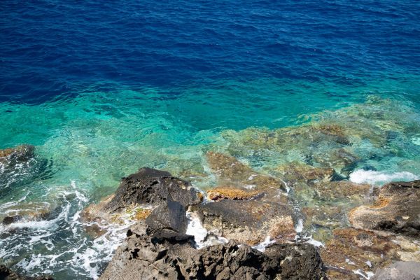 Felsen und türkisfarbenes Meerwasser an der Küste von Santorini.