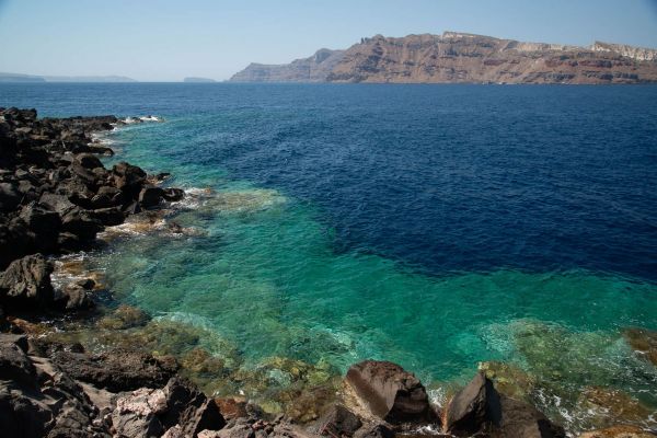 Felsküste von Santorini mit türkisfarbenem Wasser und Felsen im Hintergrund.