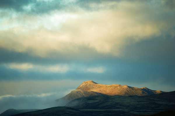 Sonnenbestrahlte Berge tauchen durch dramatische Wolken im Dovrefjell auf.