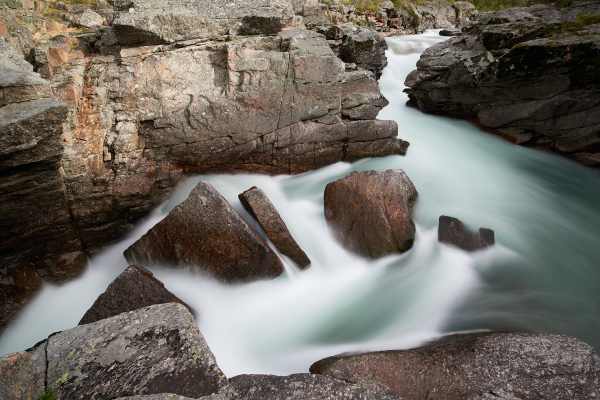Ein wilder, von Felsen umgebener Bach in Norwegen mit starker Strömung.