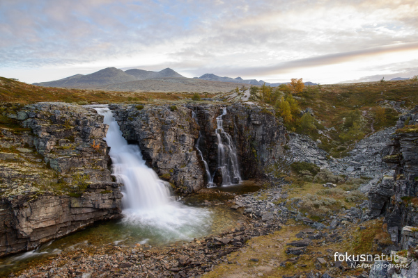 Ein Wasserfall in felsiger Umgebung im Rondane Nationalpark, Norwegen mit Bergkulisse.